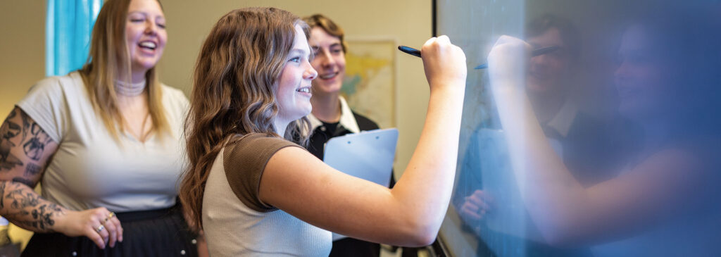 A teacher looks on as a student writes on the board