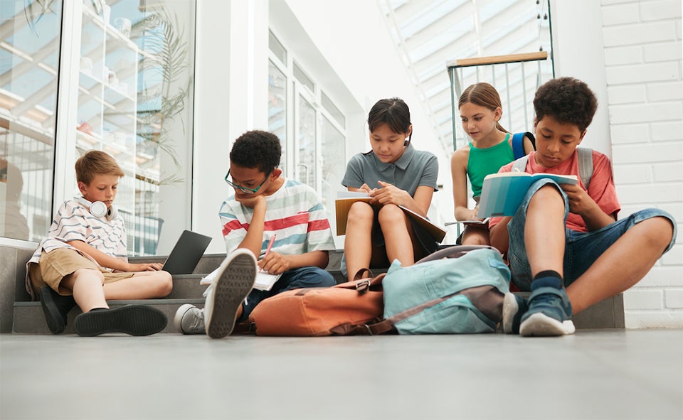 Five grade school kids sitting together on stairs writing in their notebooks.