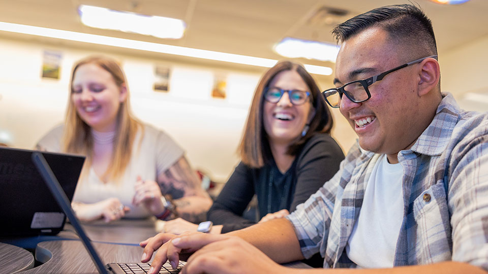 Three teachers laughing while one types on a laptop